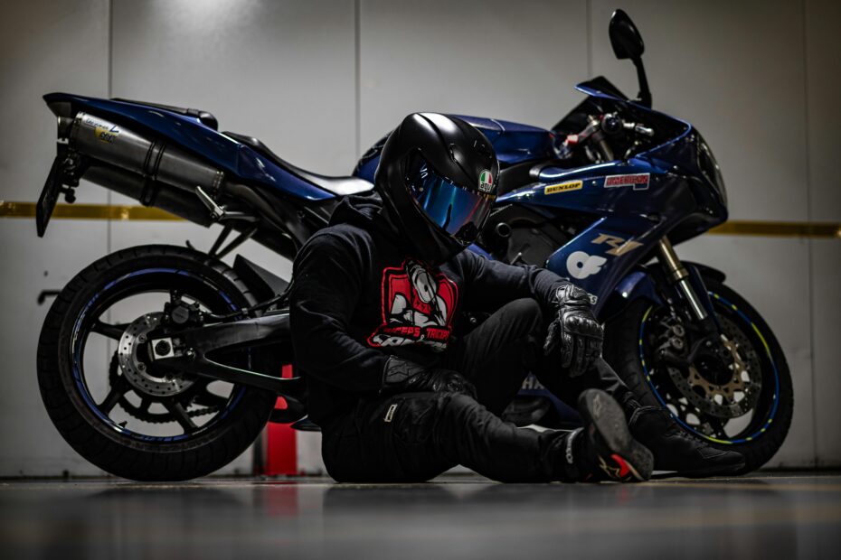 Motorcyclist in full gear sitting beside a blue sport motorcycle indoors, ready for an adrenaline ride.